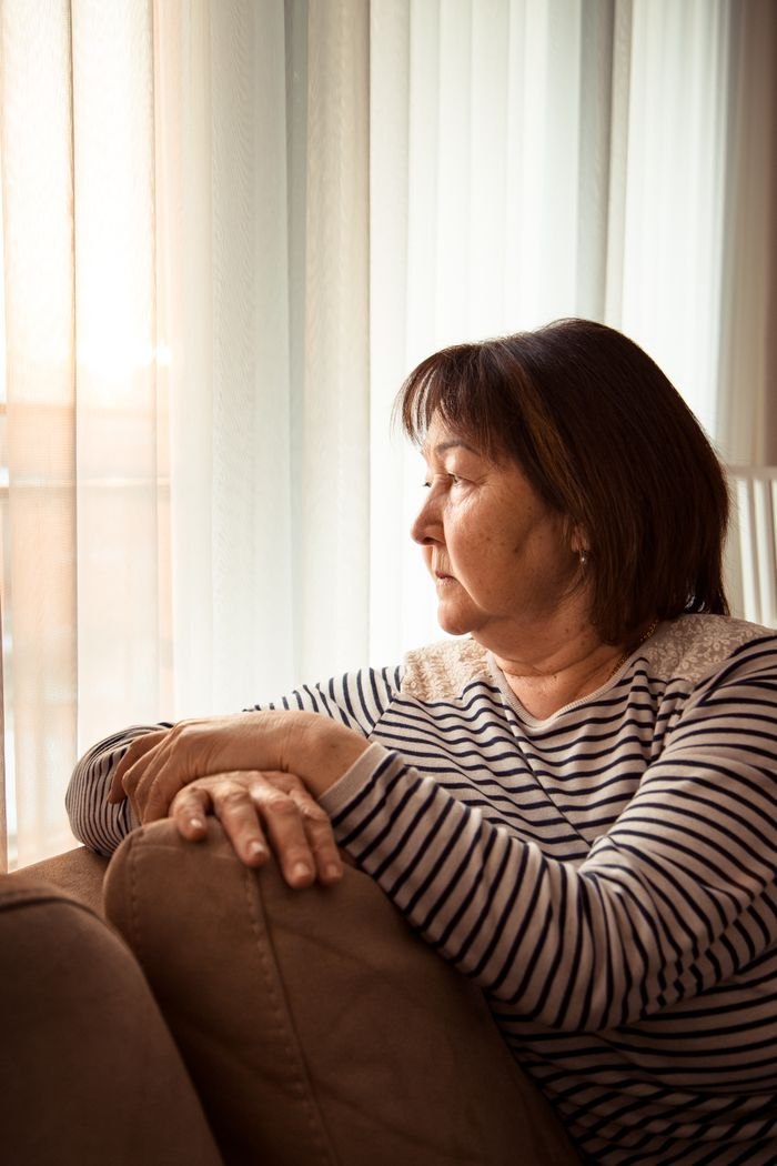 An older woman sitting quietly at home by a window