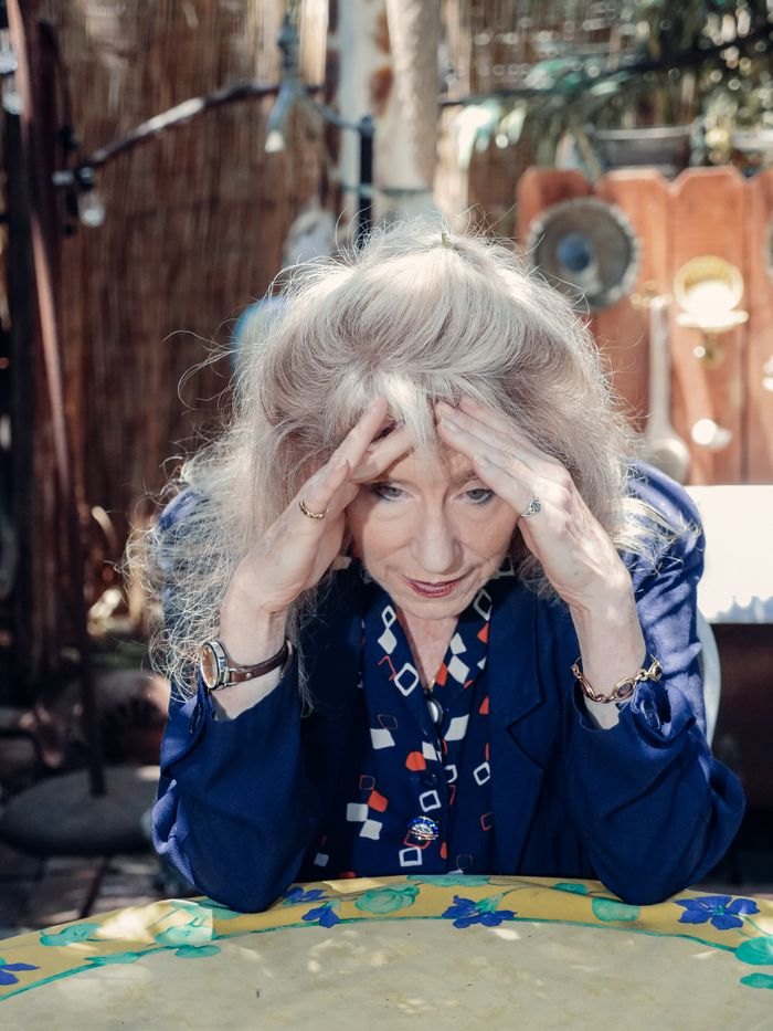 An older woman sitting alone, appearing disoriented and holding her head